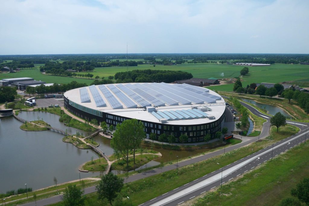 Rond gebouw met zonnepanelen omringd door groen en water.