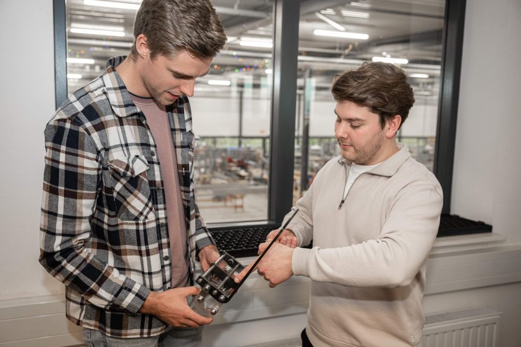 Twee mannen onderzoeken apparaat bij raam.